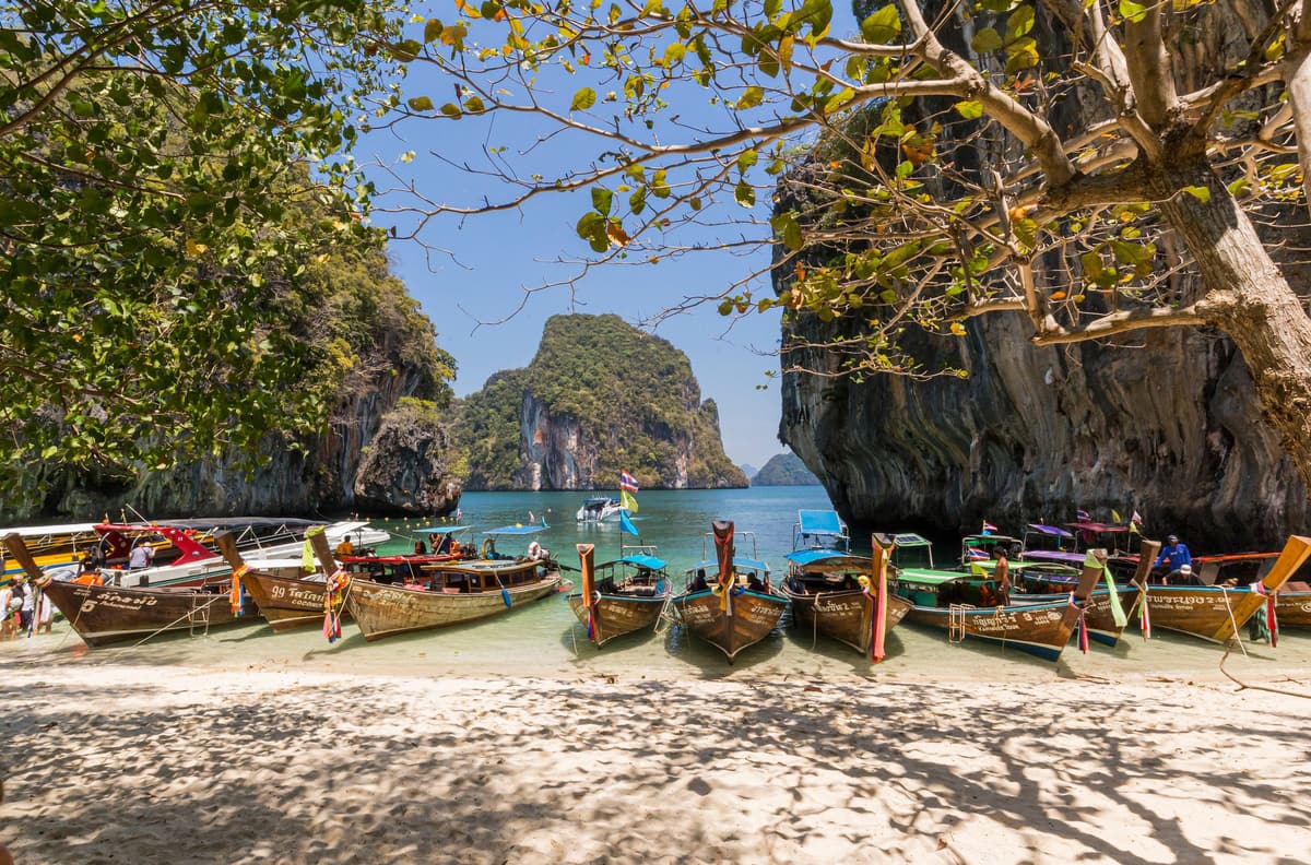 Barcas de cola larga alineadas en una playa de arena blanca, entre los picos calizos del mar de Andamán, cerca de Krabi