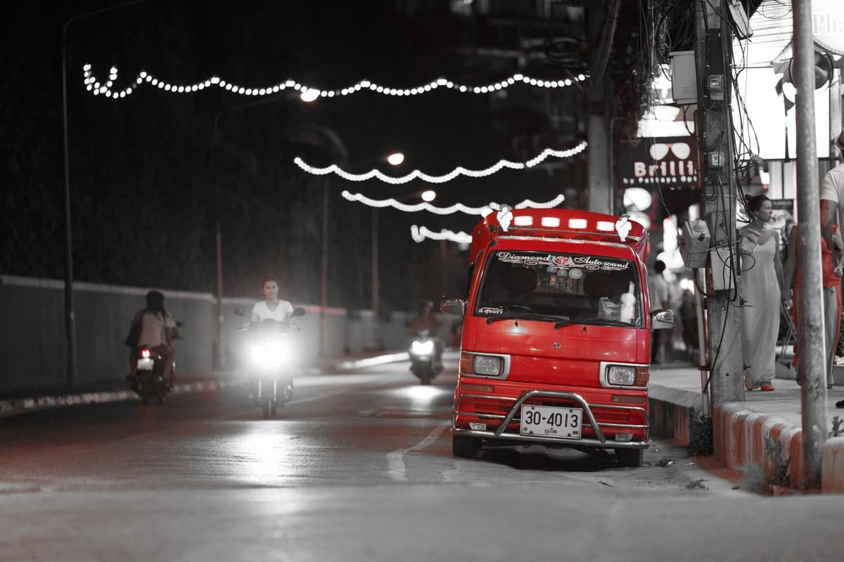 A red tuk-tuk on a Thai street at night under strings of lights