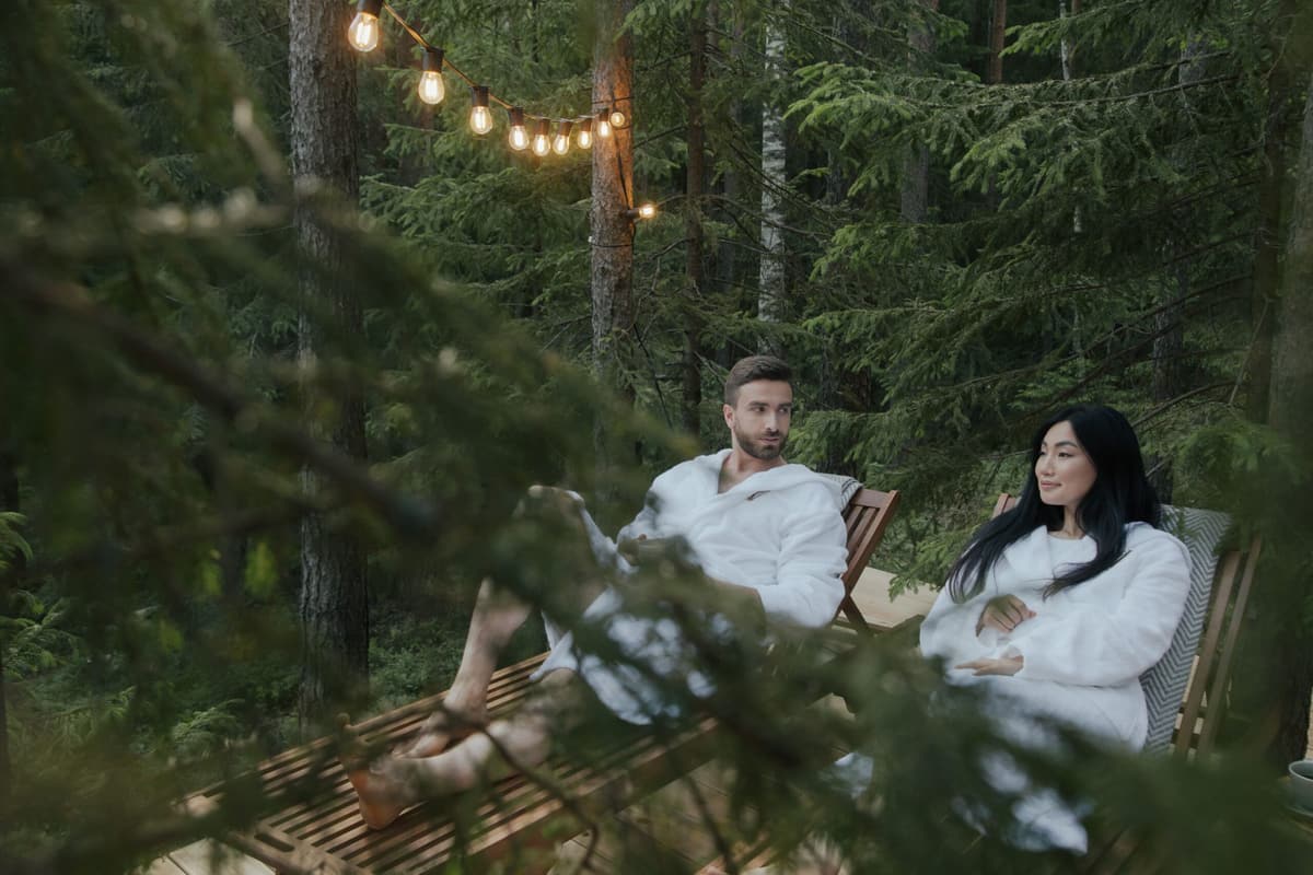Deux voyageurs se reposent sur une terrasse en forêt, sous une guirlande lumineuse