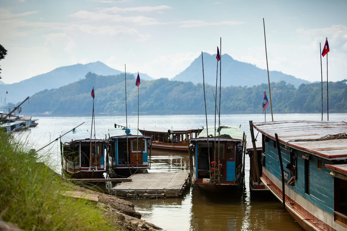 Des bateaux fluviaux en bois amarrés sur le Mékong, au pied des collines de Luang Prabang