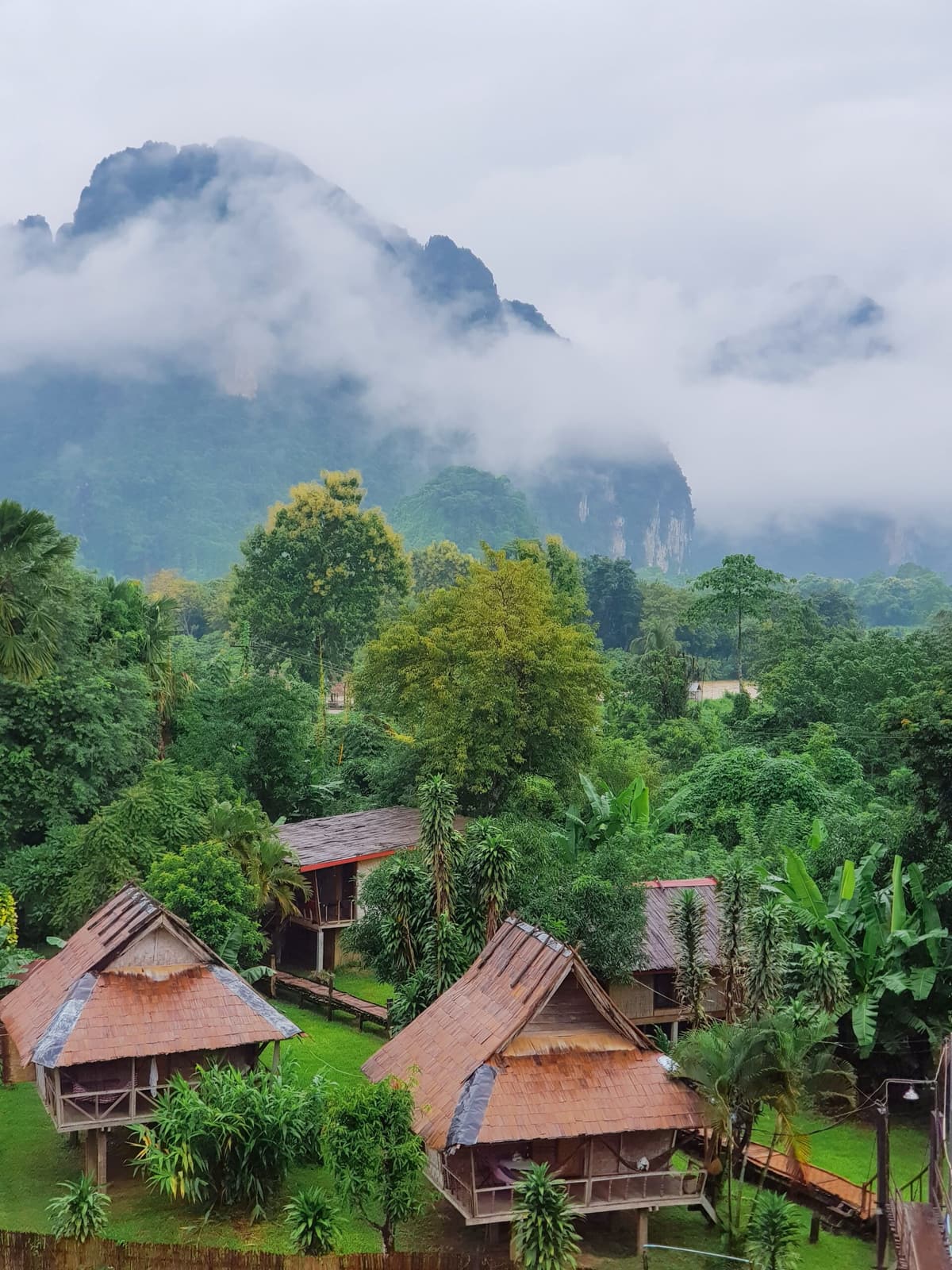 Des maisons en bois dans une vallée couverte de forêt, sous des nuages bas