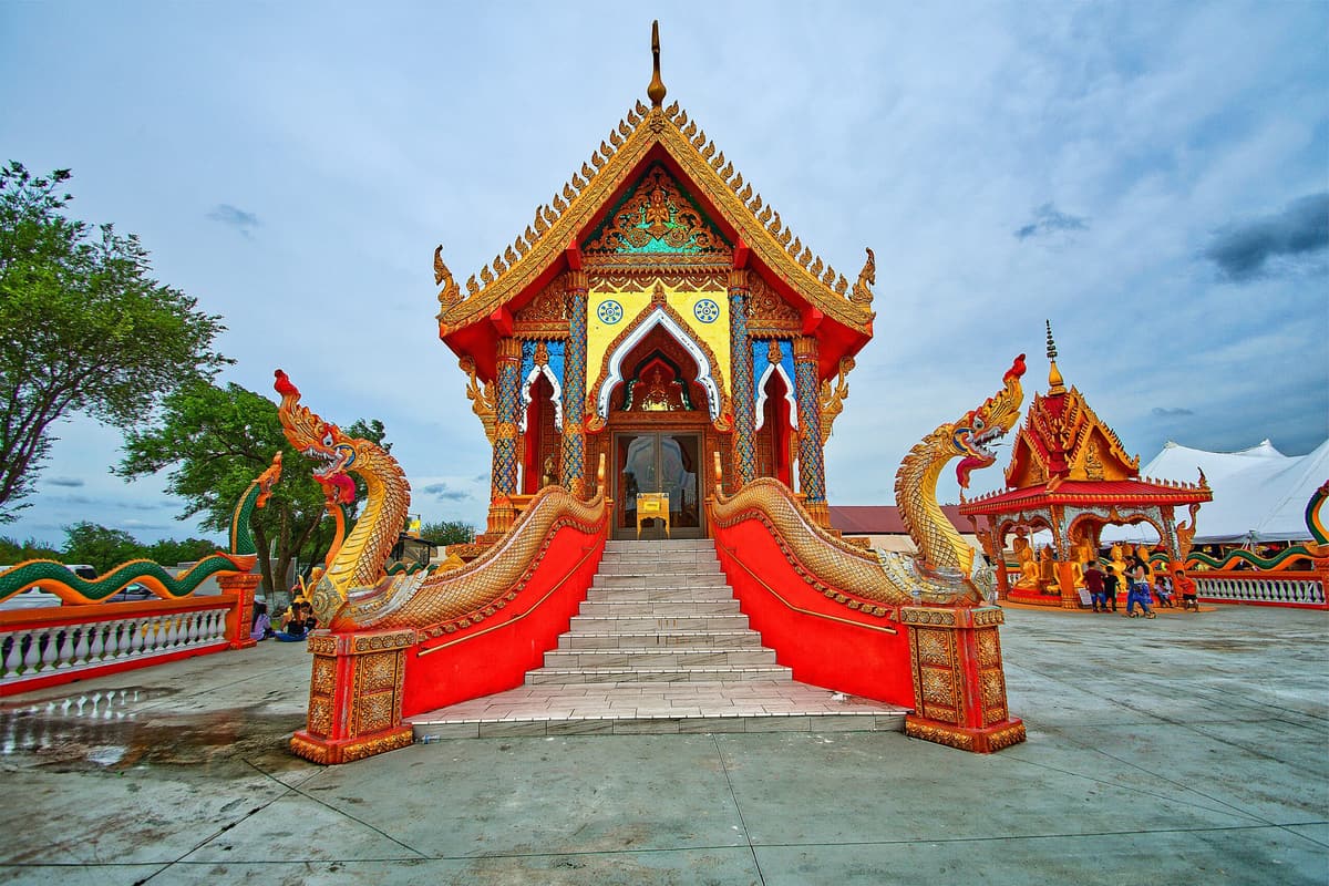 A staircase lined with red nagas leading to a gilded Thai temple