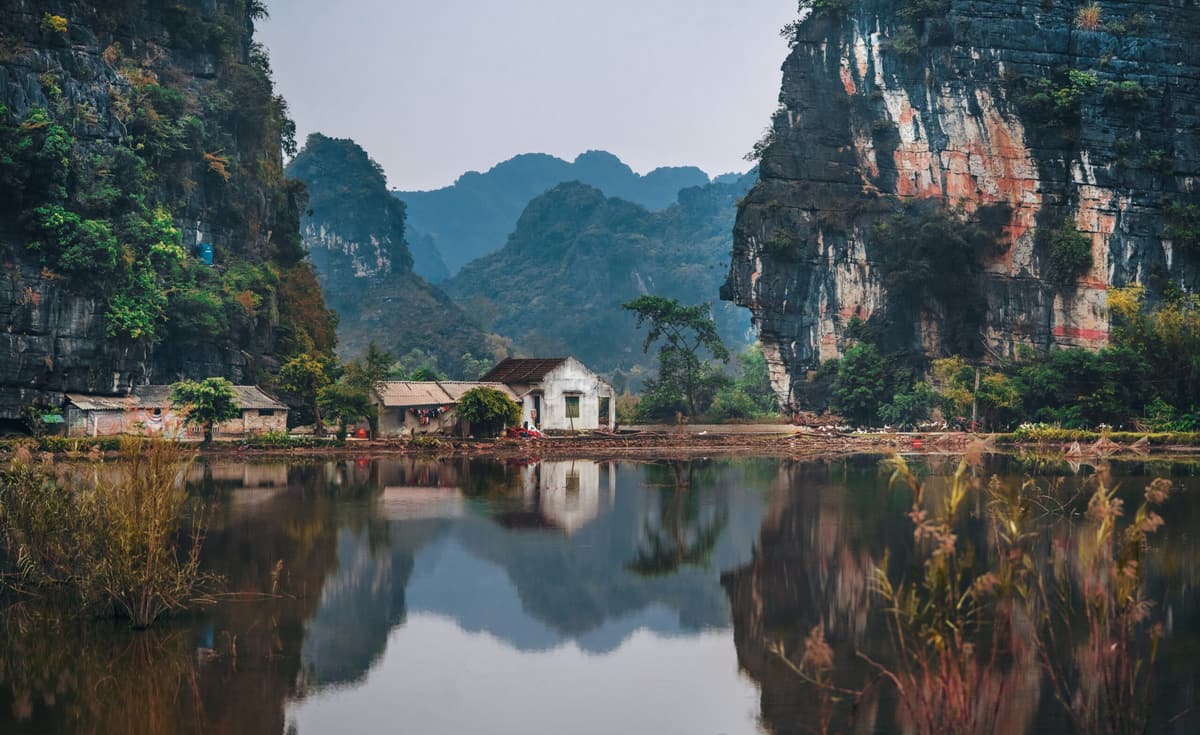 Une maison de village se reflète dans l’eau calme, sous les pitons karstiques, Ninh Binh
