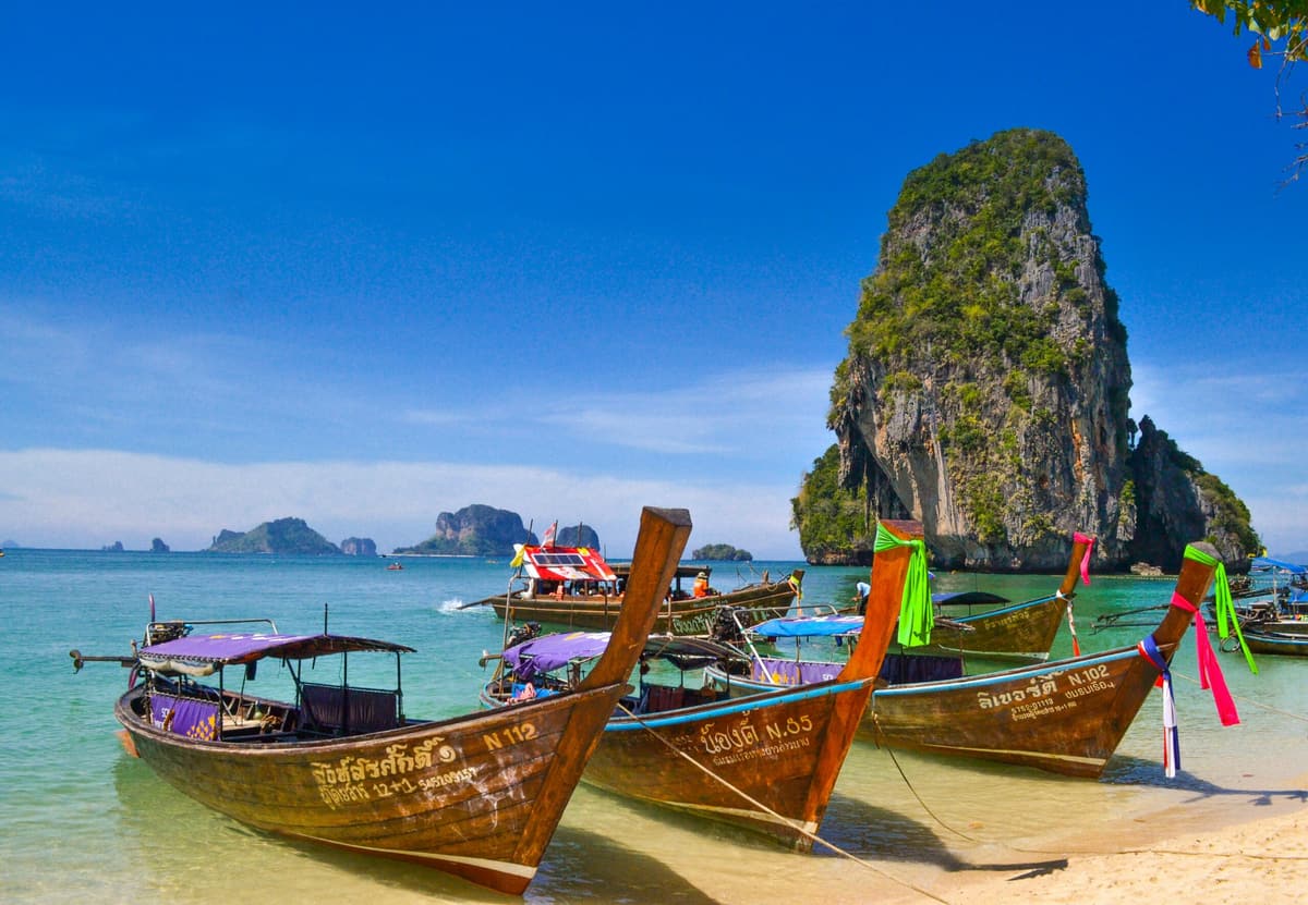 Painted long-tail boats moored on a beach below a limestone karst, Krabi